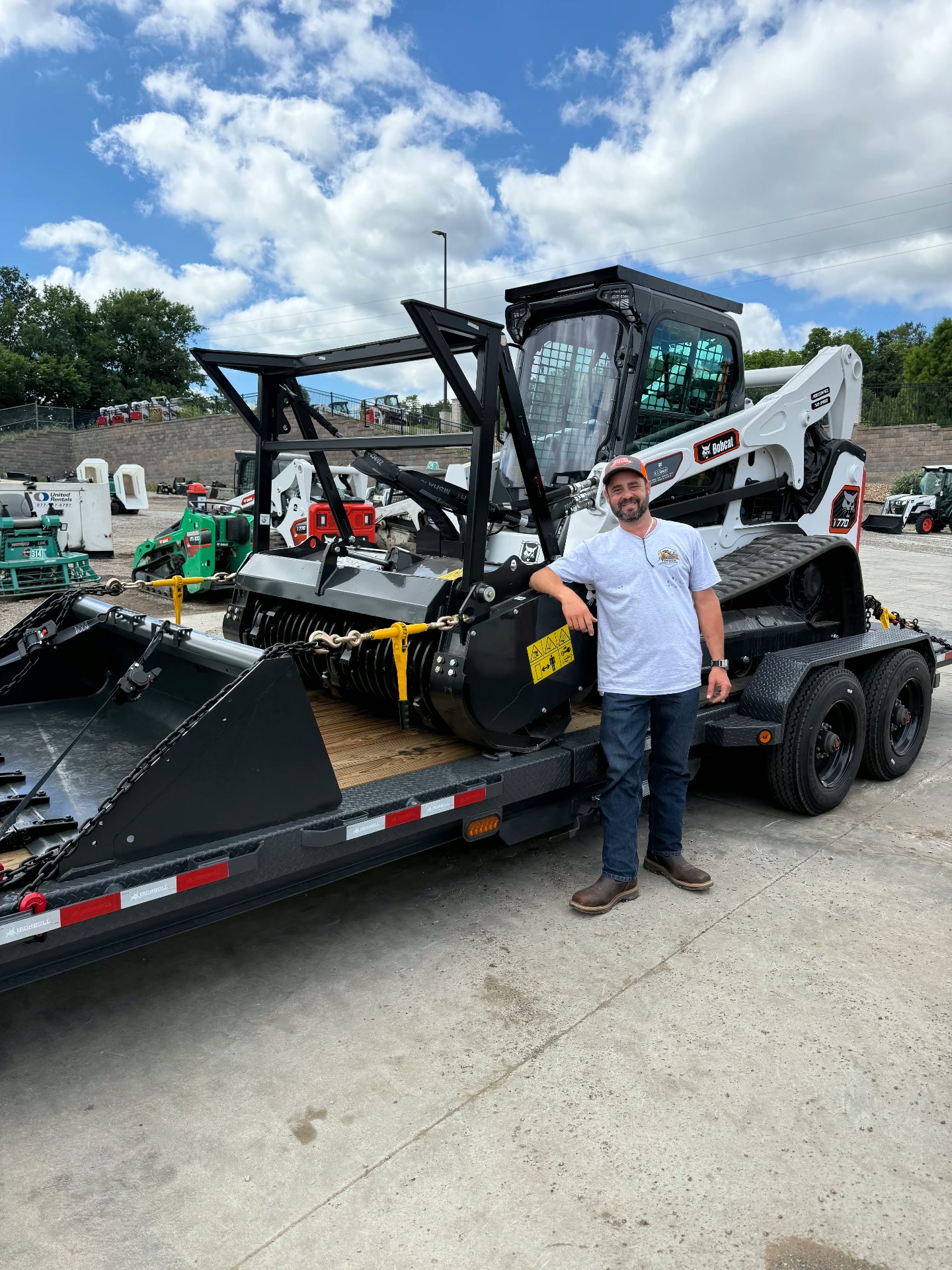 Owner standing beside the work truck and trailer carrying the Bobcat skid steer and forestry mulcher