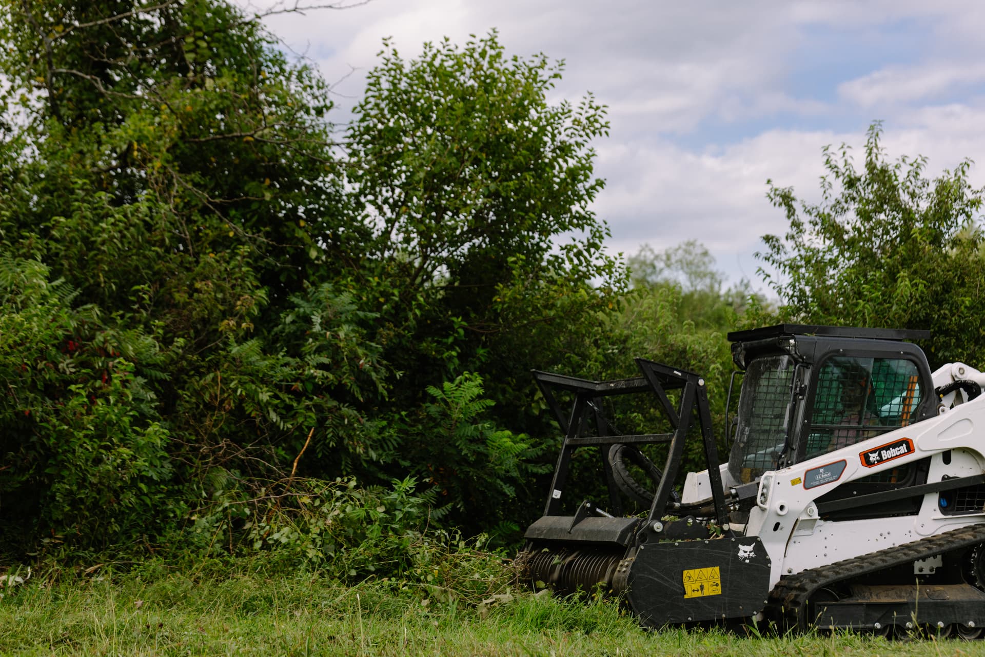 Compact track loader with a forestry mulching head clearing dense brush on rural acreage